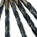 Five larger black twist drill bits fan across a white background, showing different diameters and sharp cutting tips.