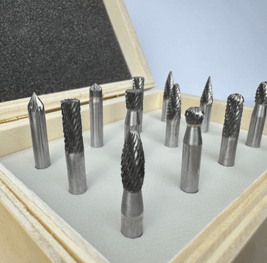Assorted carbide rotary burr bits displayed upright in an open wooden case with protective foam insert.