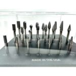 A collection of metal carbide rotary burr bits in various shapes displayed on a black stand labeled "Made in the USA."