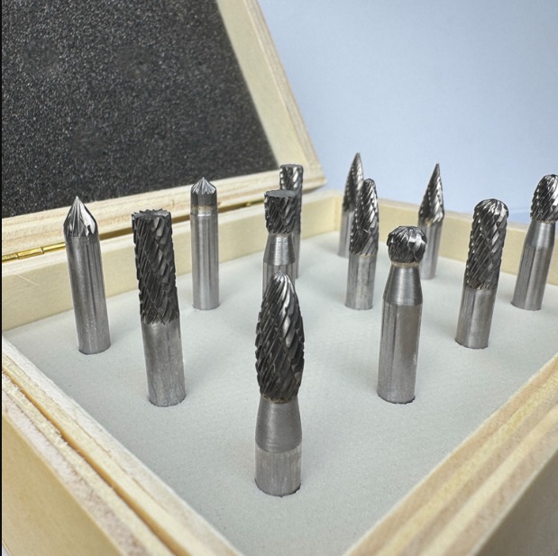 Close-up of carbide rotary burr bits with different cutting head shapes arranged in a foam-lined wooden storage case.